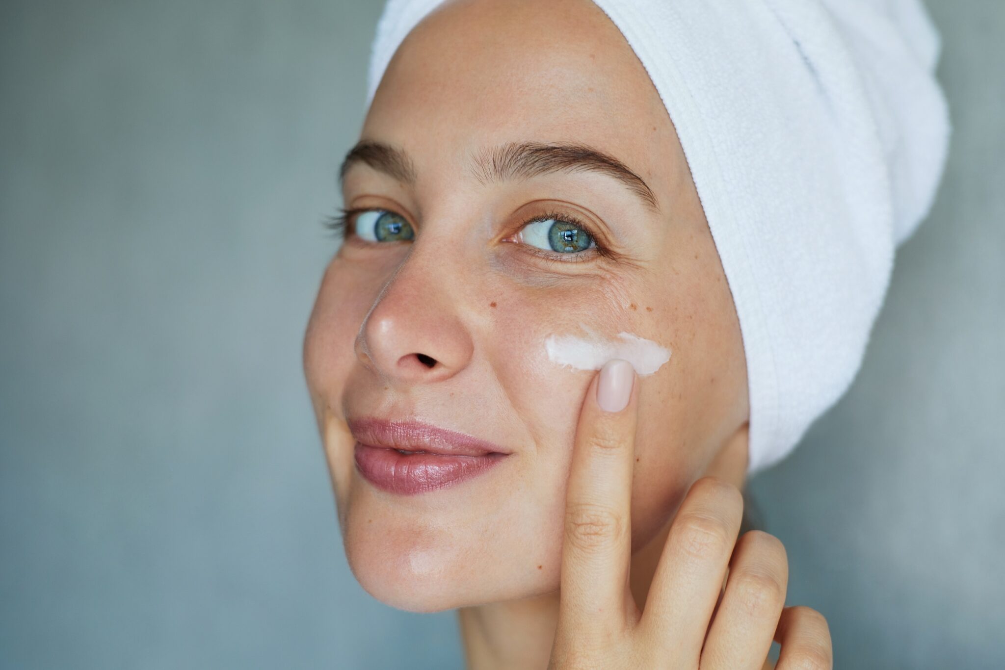 Morning skin care routine. Young beautiful woman is applying a cream, scrub beauty product on her face. Domestic daily skincare